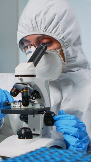 Scientist wearing ppe suit looking at samples under microscope